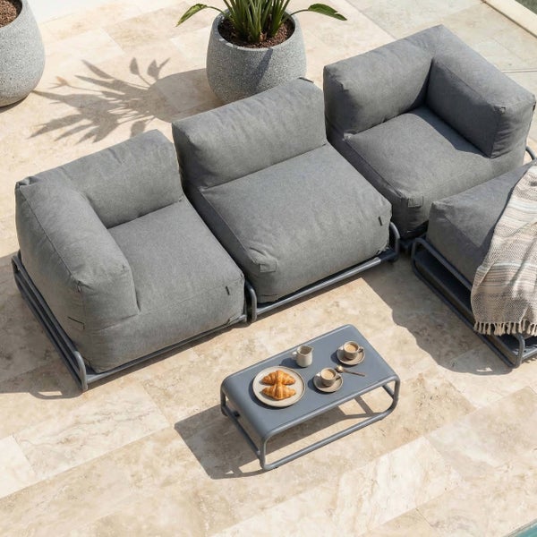 Modernes Garten-Lounge-Set mit grauen Modulsofa-Polstern, einem Metall-Couchtisch und großen Pflanzgefäßen auf einer gefliesten Terrasse.