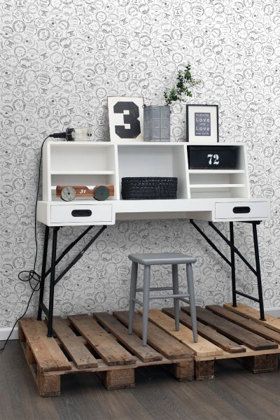 Weißer Schreibtisch mit schwarzen Metallbeinen, Ablagefächern, Dekoration und grauem Hocker auf Holzpaletten vor gemusterter Tapete
