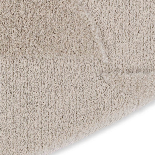 Nahaufnahme eines Hochflor-Teppichs mit geometrischem Strukturmuster und sichtbarem Teppichrücken.