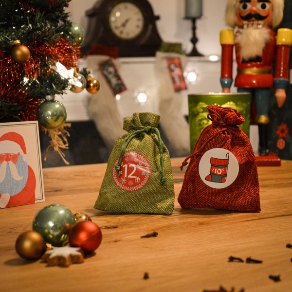 Zwei kleine Adventskalender Säckchen aus Jute auf einem Holztisch mit Weihnachtsdekoration im Hintergrund
