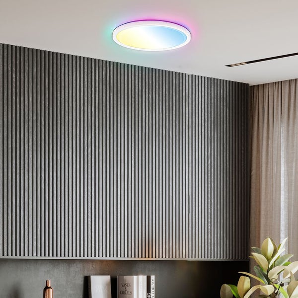 Runde LED-Deckenleuchte mit farbigem Lichtring an weißer Zimmerdecke über einer grau lamellierten Wandverkleidung in einem modern eingerichteten Raum.