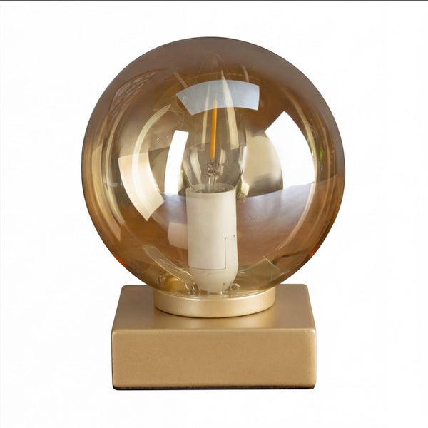 Tischleuchte mit quadratischem goldfarbenem Sockel und großer bernsteinfarbener Glaskugel mit sichtbarem Leuchtmittel.