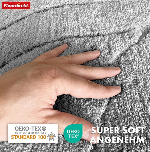 Nahaufnahme eines grauen Teppichs mit der Hand einer Person, die die weiche Textur berührt, mit dem Floor direkt Logo und dem OEKO-TEX Siegel.