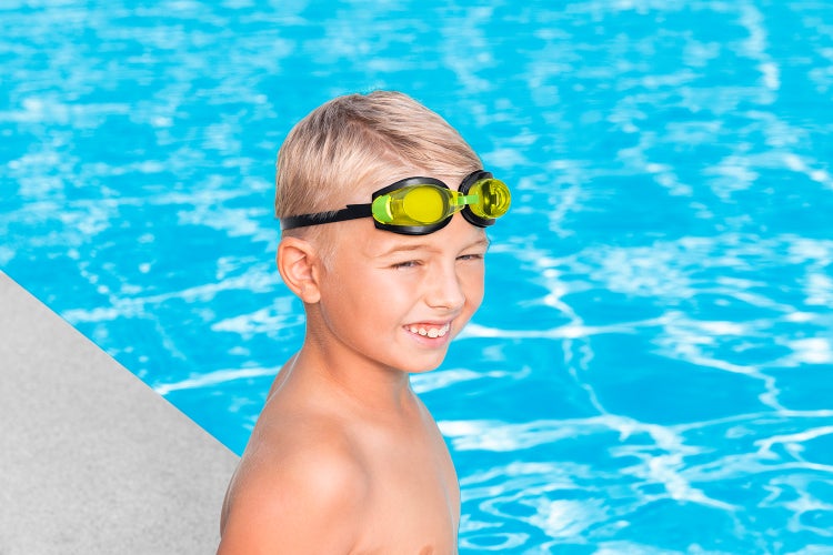 Ein lächelndes Kind mit Schwimmbrille am Rand eines hellen Schwimmbeckens.