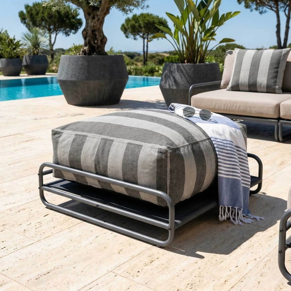 Gestreifter Outdoor-Hocker mit Metallgestell, Handtuch und Sonnenbrille auf einer hellen Terrasse am Pool, umgeben von Pflanzenkübeln.