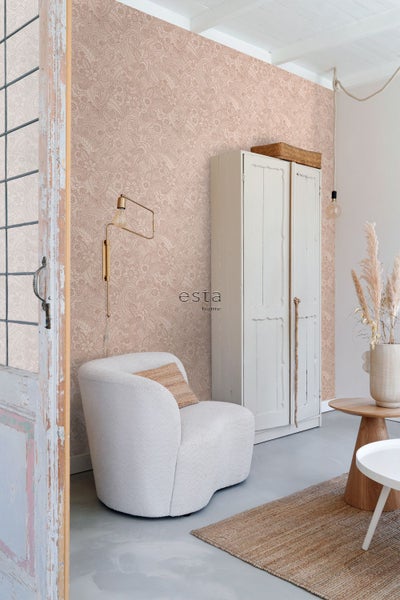Wohnraum mit floral gemusterter Tapete, weißem Sessel, Vintage-Schrank und goldener Wandleuchte. esta home Logo.