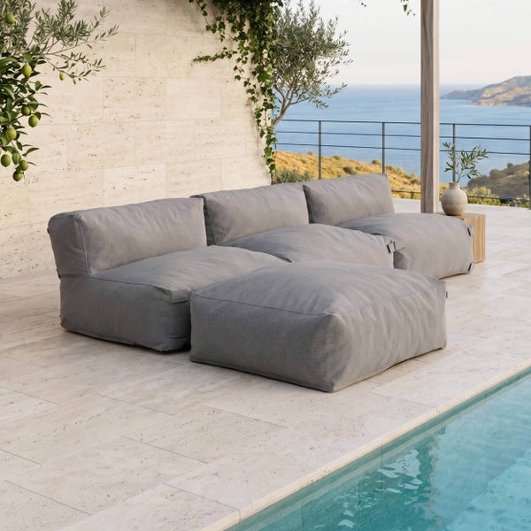 Moderner grauer modularer Outdoor-Lounge-Sofa auf einer hellen Terrasse mit Pool und Meerblick.