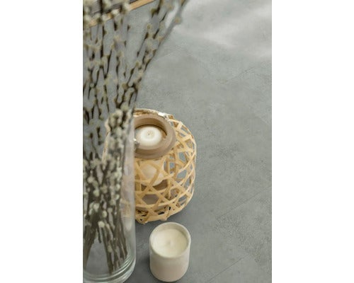 Dekorative Elemente auf einem Bodenbelag, darunter Zweige in einer Vase, Windlicht und Kerze.