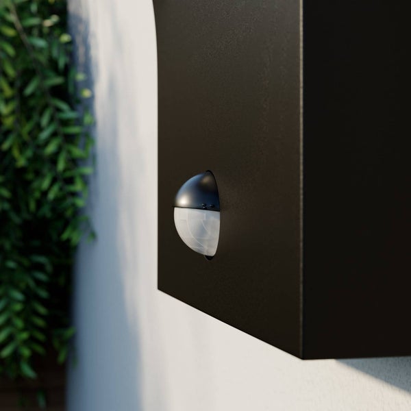 Nahaufnahme einer schwarzen Außenwandleuchte mit integriertem Bewegungsmelder an einer Hauswand.