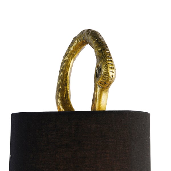 Detailansicht einer Lampe mit schwarzem Lampenschirm und goldfarbener Verzierung in Form eines Vogelkopfes