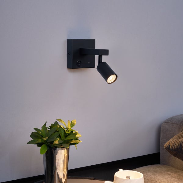 Schwarze Wandleuchte mit USB-Anschluss über einem Beistelltisch mit Pflanze