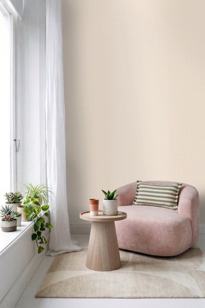Vliestapete mit Karomuster in einem hellen Zimmer mit Sessel, Holzbeistelltisch, Zimmerpflanzen auf dem Fensterbrett und Vorhang.