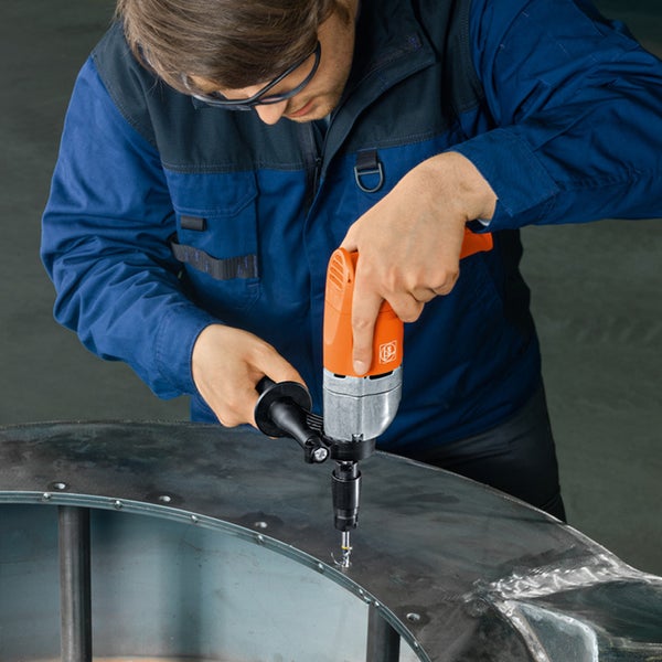 Mann bohrt mit einer Fein Bohrmaschine ein Loch in ein Metallstück