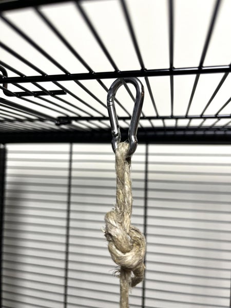 Metall-Karabinerhaken mit einem verknoteten Seil aus Naturfaser, befestigt an den Gitterstäben eines Käfigs.