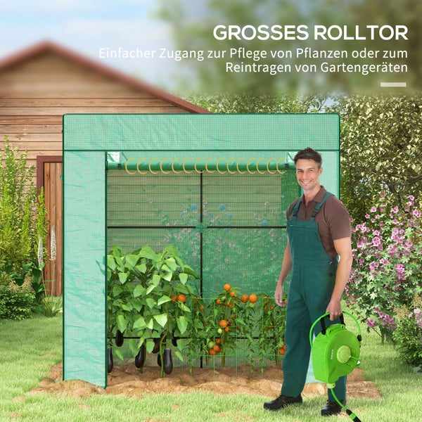Ein Folien-Gewächshaus mit aufrollbarem Tor steht im Garten, daneben ein Mann mit einer Gartenschlauchbox vor einem Holzhaus.