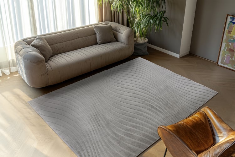 Wohnzimmer mit einem rechteckigen Teppich mit Wellenmuster vor einem Sofa, einem Sessel und einer Pflanze auf einem Parkettboden.