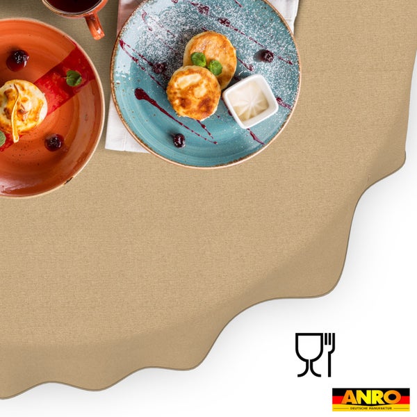 Beige Tischdecke mit Wellenrand und Textilstruktur, gedeckt mit Tellern und Speisen, lebensmittelecht, ANRO Logo.