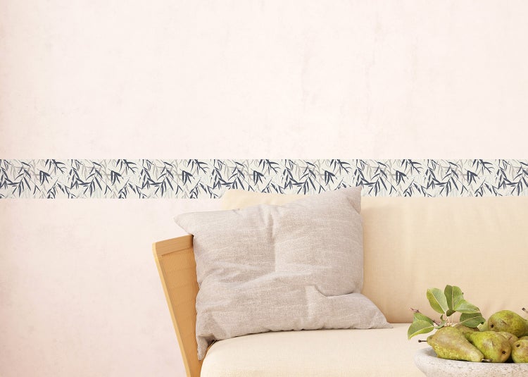 Wandbordüre mit Bambusblatt-Muster an einer Wand über einem Sofa mit Kissen in einem hellen Wohnzimmer.