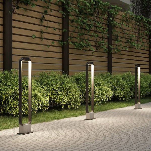 Moderne LED-Sockelleuchten mit offenem rechteckigem Rahmen beleuchten einen gepflasterten Gartenweg entlang einer Hecke und Holzwand.