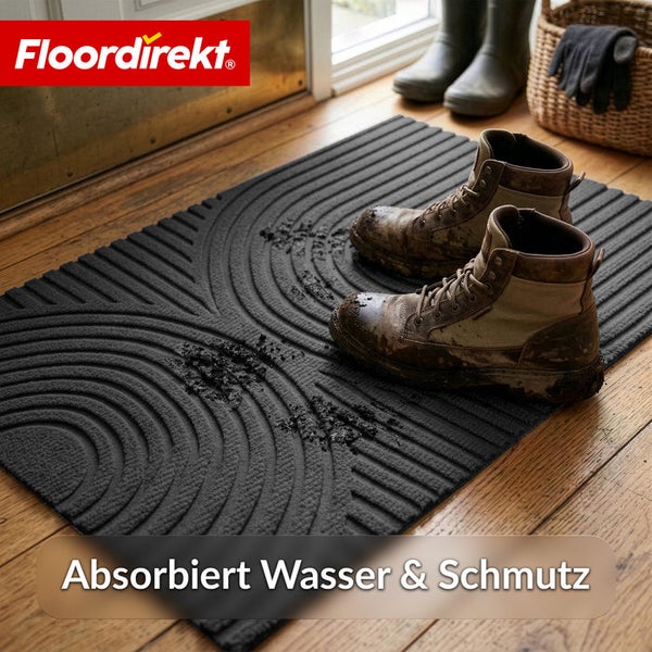 Schmutzfangmatte von Floordirekt mit Rillenprofil auf Holzboden, absorbiert Wasser und Schmutz, Arbeitsstiefel darauf. Floordirekt Logo.