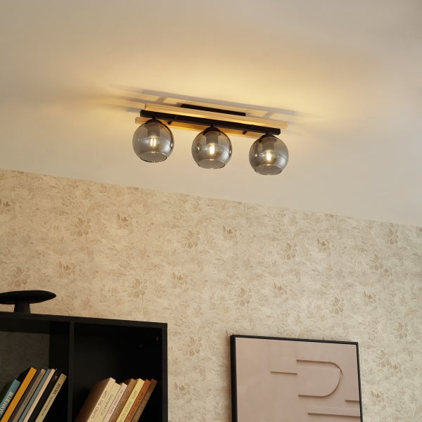 Moderne Deckenleuchte mit drei gläsernen Kugelschirmen montiert an einer Holzschiene an der Decke.