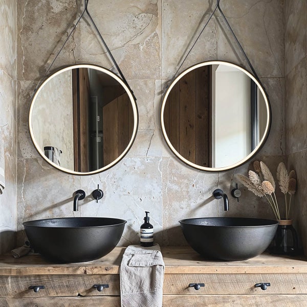 Badezimmer mit zwei runden Spiegeln mit Beleuchtung, zwei schwarzen Aufsatzwaschbecken und einem Waschtisch aus Holz