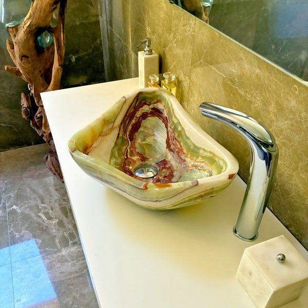 Naturstein-Aufsatzwaschbecken aus Onyx auf einem weißen Waschtisch mit verchromter Armatur in einem modernen Badezimmer.