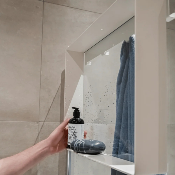 Ein moderner Badezimmerspiegel mit integrierter Ablagefläche, auf der ein Seifenspender und ein Seifenstück stehen, daneben ein Handtuch.