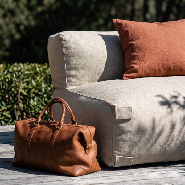 Outdoor-Lounge-Sessel aus strukturiertem Stoff mit einem Kissen und einer Ledertasche auf einer Holzterrasse im Garten.