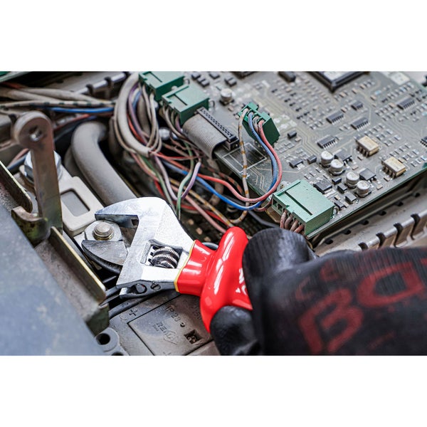 Eine Hand mit Handschuh benutzt einen verstellbaren Schraubenschlüssel an einer elektronischen Komponente.