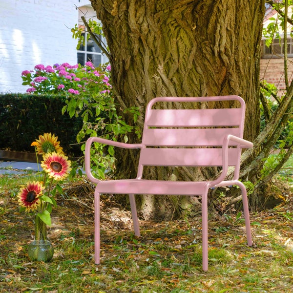 Moderner Gartenstuhl aus rosa Metall mit Armlehnen und Latten-Design, platziert in einem Garten unter einem Baum neben Sonnenblumen.