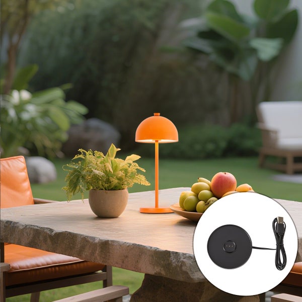 Orangefarbene, wiederaufladbare LED-Tischleuchte für außen in Pilzform auf einem Gartentisch, inklusive USB-Ladestation.