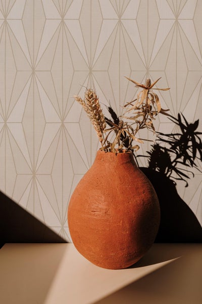 Terrakotta Vase mit Trockenblumen vor einer Vliestapete mit geometrischem Rautenmuster in einem modern gestalteten Wohnraum.