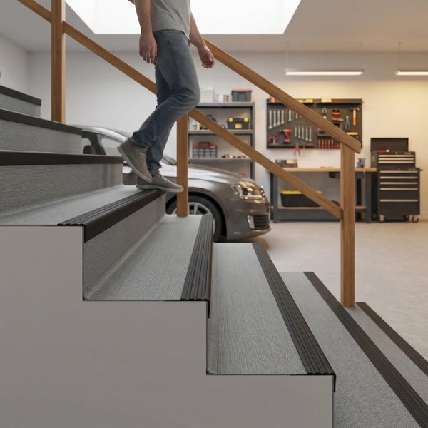 Eine Person geht eine Treppe mit Treppenkantenprofilen in einer organisierten Werkstatt mit Auto, Werkbank und Werkzeugwand hinunter.
