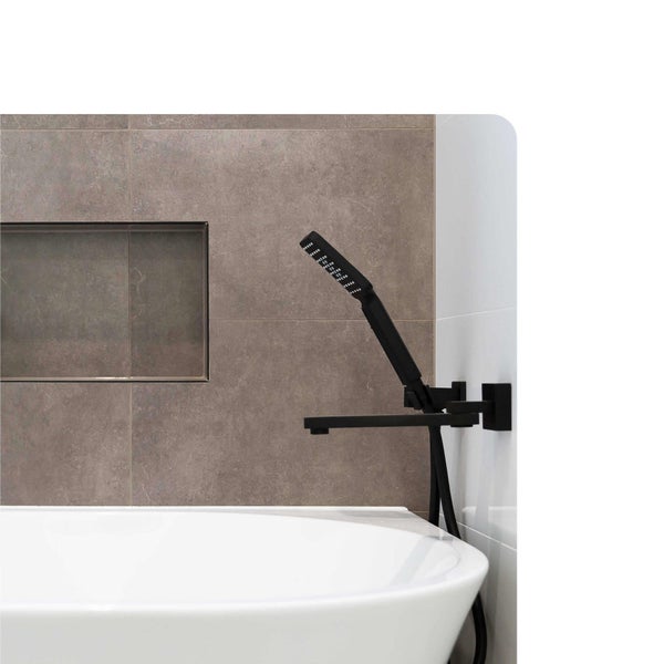 Schwarze Badewannenarmatur zur Wandmontage mit Handbrause, installiert in einem Badezimmer mit grauen Fliesen, Wandnische und weißer Badewanne.