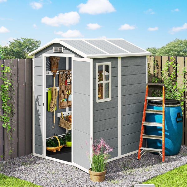 Gartenhaus mit Satteldach und offener Tür, eingerichtet mit Werkzeugwand und Regalen, im Garten auf einer Kiesfläche mit Leiter und Regentonne.