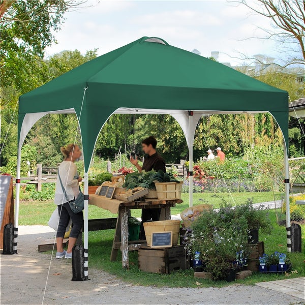 Grüner Faltpavillon mit weißem Gestell auf einem Gartenmarkt, inklusive Standfüßen mit Gewichten für Stabilität.