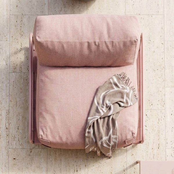 Rosafarbener Sessel in der Draufsicht mit einer gemusterten Decke auf Steinboden.