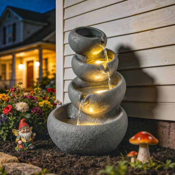 Gartenbrunnen mit vier Schalen aus wetterfestem Kunstharz in Steinoptik und LED-Beleuchtung in einem bepflanzten Garten