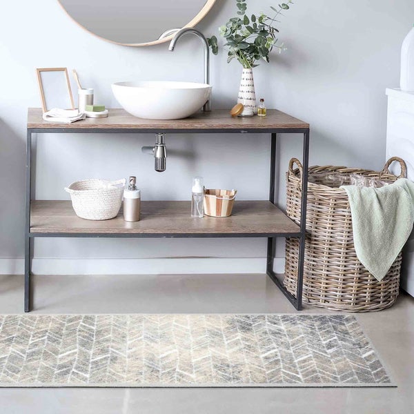 Helles Badezimmer mit Waschbecken auf einem Regal mit zwei Ebenen, einem runden Spiegel, einem Wäschekorb und einem Teppich mit Zickzackmuster.