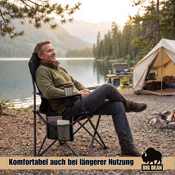 Ein Mann sitzt in einem bequemen Campingstuhl mit Getränkehalter und Seitentasche vor einem Zelt am See in einer malerischen Naturlandschaft.