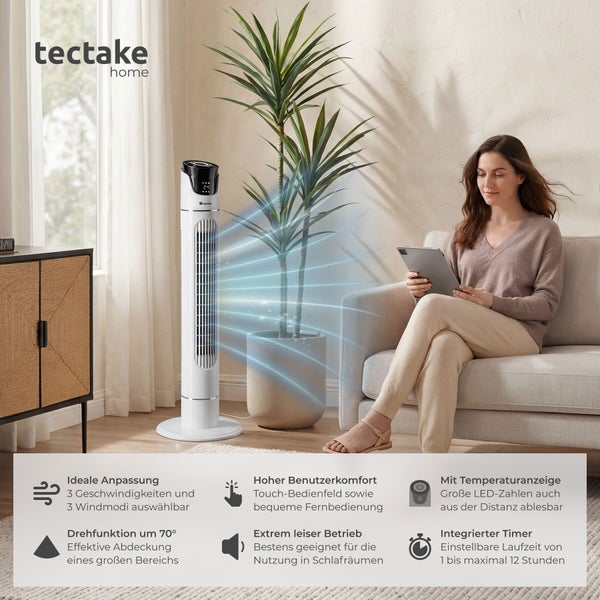 Weißer tectake home Turmventilator in einem hellen Wohnzimmer neben einer Zimmerpflanze, während eine Frau auf einem Sofa sitzt.