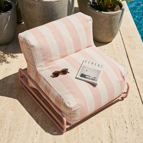Gestreifter Lounge-Sessel auf Metallgestell auf einer hellen Terrasse am Pool mit Pflanzkübeln aus Beton.