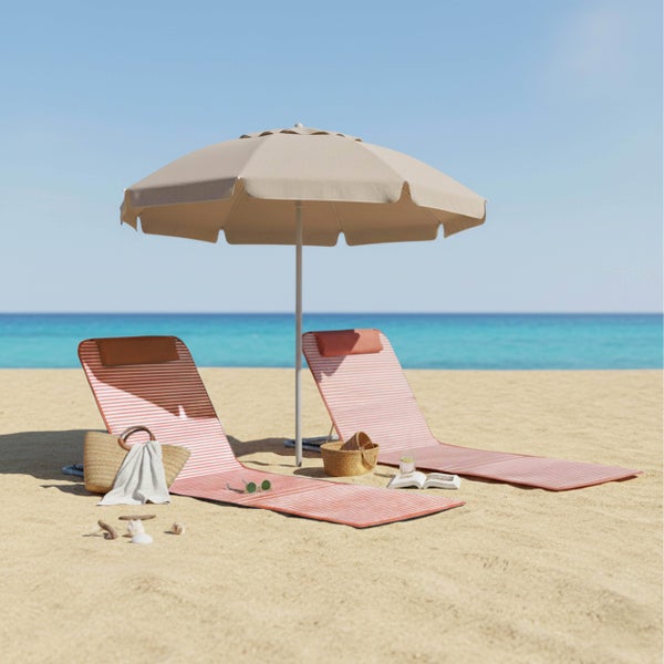 Zwei gestreifte Strandmatten und ein beiger Sonnenschirm auf einem sandigen Strand vor blauem Meer und klarem Himmel mit Strandzubehör.