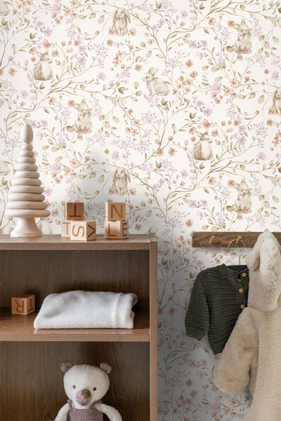 Helle Tapete mit Hasen- und Blumenmuster in einem organisierten Kinderzimmer mit Holzregal, Holzspielzeug und Kinderkleidung.