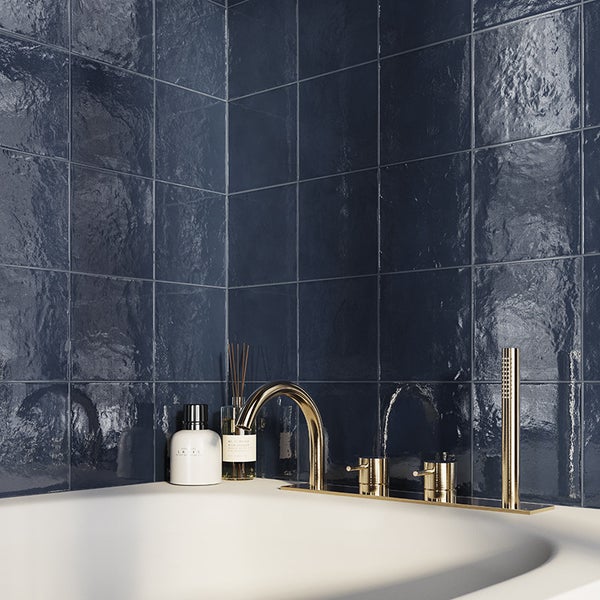 Badezimmer mit dunkelblauen, glänzenden Wandfliesen in quadratischer Optik und goldfarbener Wannenarmatur an einer weißen Badewanne.