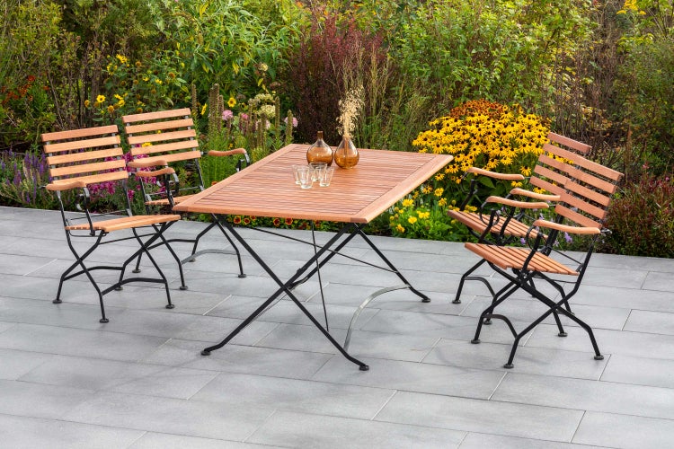 Gartenmöbelset mit Holztisch und vier Klappstühlen vor blühendem Garten
