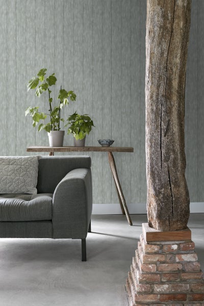 Wohnzimmer mit Sofa, Tisch mit Pflanzen und einer Holzsäule vor einer Tapete mit Holzstruktur