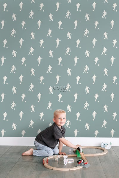 Helle und einladende Szene mit einer Tapete mit Fußballmotiven, einem spielenden Kind und einer Holzeisenbahn.