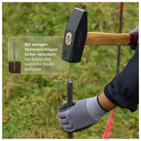 Ein Hammer treibt einen Metallstab für eine stabile Verankerung im Gartenboden ein.